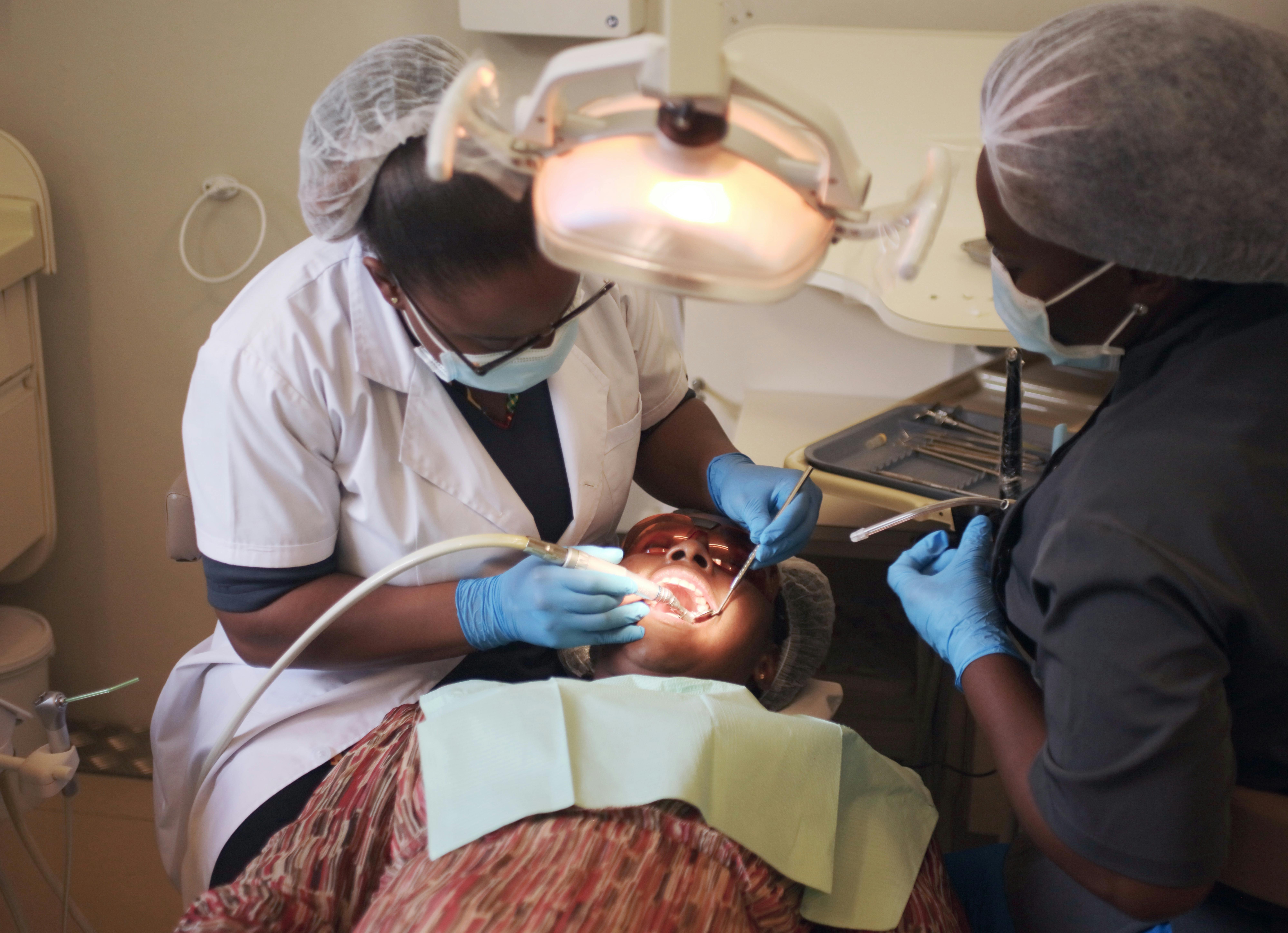 Dentist in blue scrubs examining patient in modern dental chair with bright overhead light