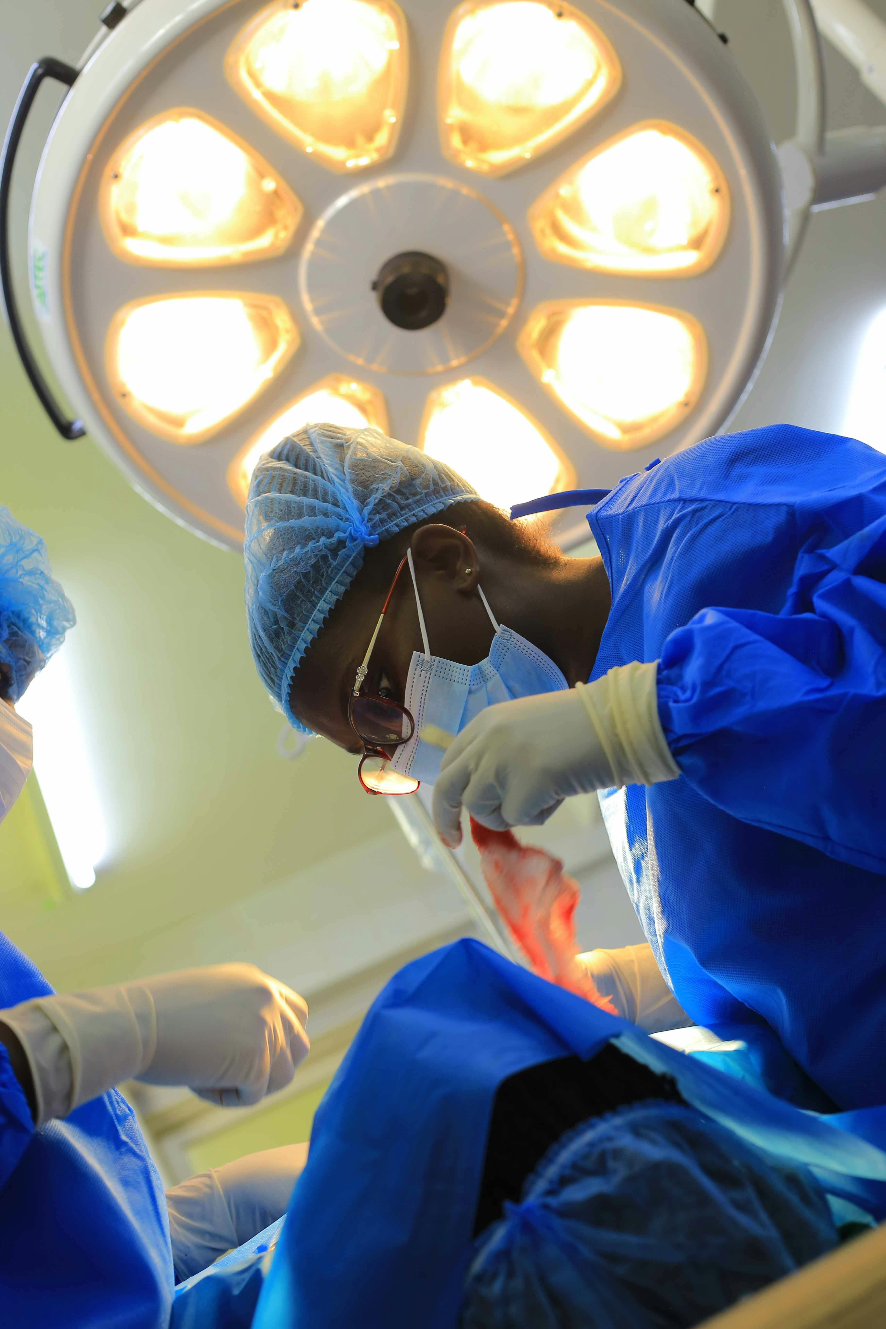 Surgeon in green scrubs and gloves performing minor procedure in clean operating room bright overhead light